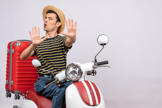 轻便摩托车一个不高兴的年轻人戴着草帽坐在轻便摩托车上做停车标志的正面图稻草成人人