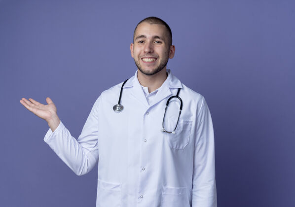 周围面带微笑的年轻男医生身穿医用长袍 脖子上戴着听诊器 紫色的墙上孤立着一只空手医学人表情