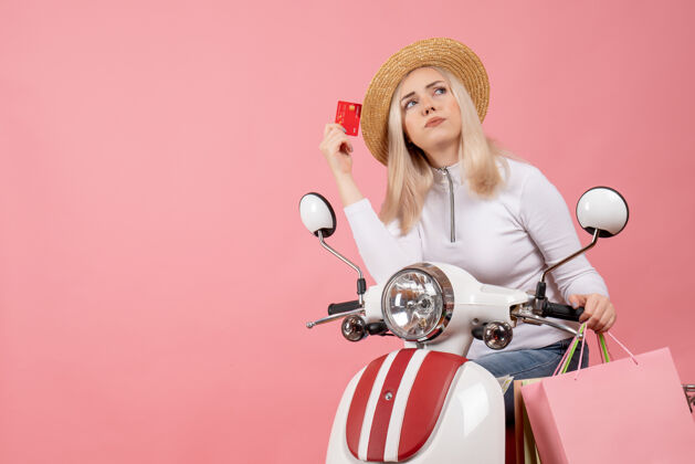 坐着前视图坐在轻便摩托车上拿着信用卡的年轻女士在想什么轻便摩托车前面帽子