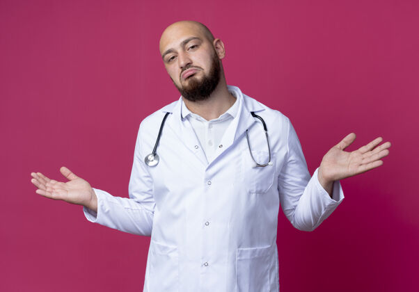 长袍困惑的年轻男医生穿着医用长袍和听诊器摊开双手听诊器粉红色医生