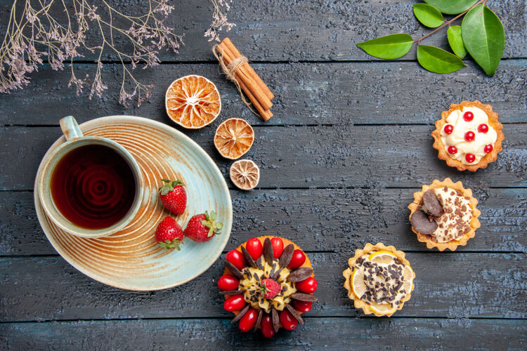 蛋糕顶视图一杯茶和草莓放在茶碟上干橙子馅饼叶子肉桂和草莓蛋糕放在深色木桌上杯子热的木头