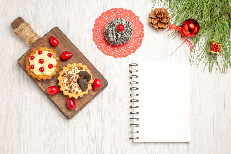 书签俯瞰砧板上的可可 浆果馅饼和山茱萸可可蛋糕和松树叶子 还有白色木质地面上的圣诞玩具和笔记本松树圣诞树笔记本
