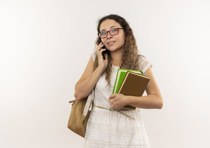 人高兴的年轻漂亮的女学生戴着眼镜 背着书包 在白墙上讲电话衣服女生眼镜