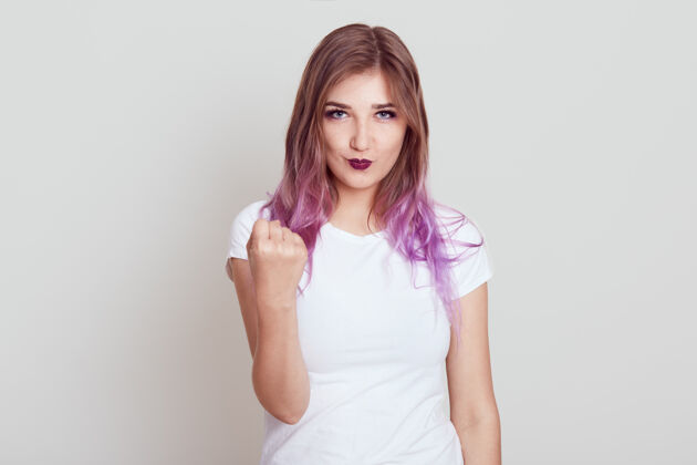 人严格严肃的女性 淡紫色头发 穿着白色t恤 露出愤怒的表情 警告做坏事 在灰色的墙上摆出孤立的姿势随意专横年轻