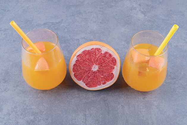 水果在灰色背景上拍摄新鲜橙汁和成熟葡萄柚的特写照片五个玻璃杯餐桌
