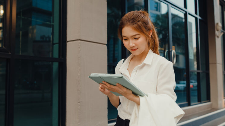 高管成功的亚洲年轻女商人穿着时尚的办公服 使用数码平板电脑和打字短信步行自信应用程序