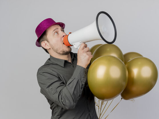 壁板快乐的年轻人戴着粉红色的帽子拿着气球在白色的喇叭上讲话说话帽子派对