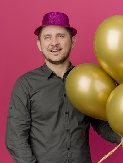 帽子微笑的年轻人戴着粉红色的帽子拿着气球孤立在粉红色的聚会派对粉色抱着