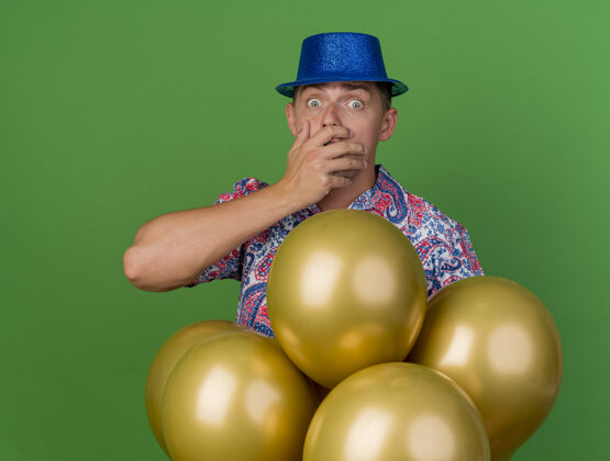 掩护一个戴着蓝色帽子的年轻人站在气球后面 一只手捂着脸 一只手被绿色隔离气球穿上脸