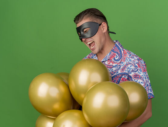 关闭快乐的年轻人闭着眼睛戴着化装眼罩拿着气球孤立在绿色派对派对绿色家伙