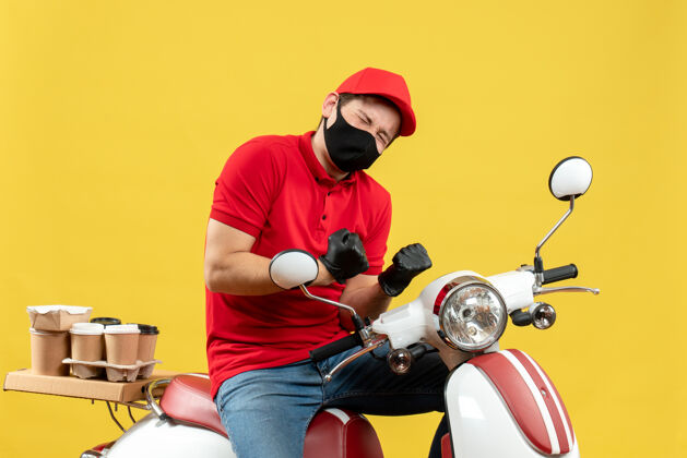 摩托车俯视图：身穿红色上衣 戴着帽子手套 戴着医用面罩 坐在滑板车上传递订单的快乐快递员体育医疗面罩