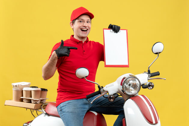 人前视图的快递员身穿红色上衣 戴着帽子手套 戴着医用口罩 坐在摩托车上拿着文件递送订单运动摩托车面罩