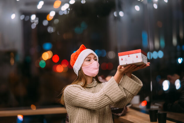 圣诞帽肖像快乐的年轻美女拿着礼品盒微笑在咖啡馆咖啡馆礼物肖像
