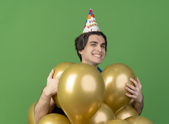 穿高兴的帅哥戴着生日帽 手里拿着隔离在绿墙上的氦气球氦人姿势