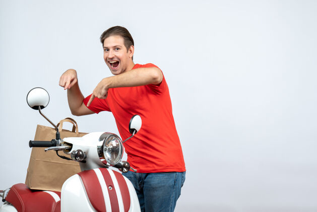 男人正面图是微笑的送货员 身穿红色制服 站在踏板车旁 在白色背景上指着订单近男性人物