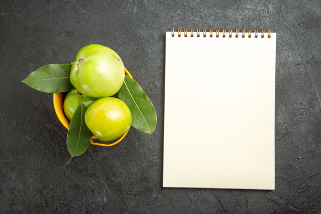水果顶视图桶绿色西红柿和月桂叶和一个笔记本在黑暗的背景柠檬农产品可食用水果