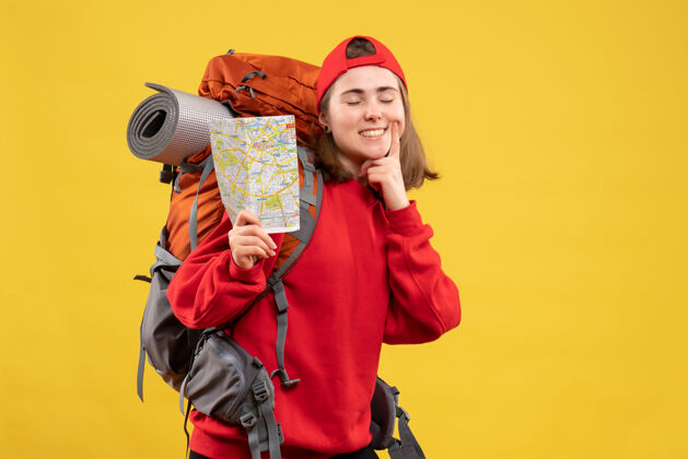 女士正面图微笑的女露营者与红色背包举行地图正面背包帽子