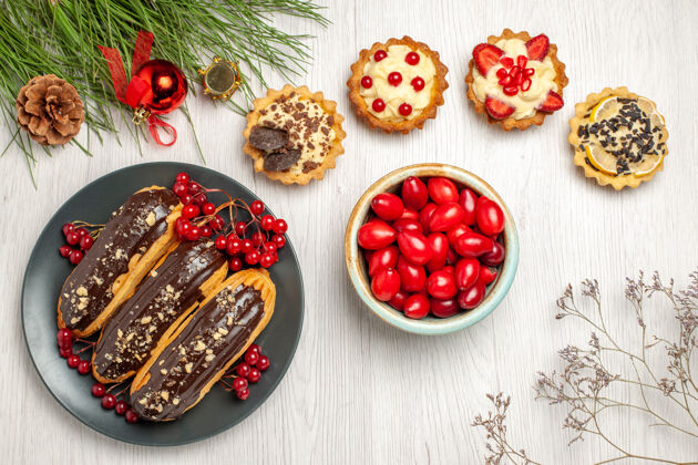 碗顶视图：灰色盘子上的巧克力蛋糕和葡萄干馅饼一碗山茱萸和松叶 上面放着圣诞玩具盘子午餐玩具