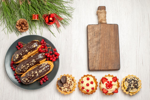 馅饼俯瞰图：灰色盘子上的巧克力蛋糕和葡萄干一个砧板馅饼和松叶 白色木质地面上有圣诞玩具木板地盘子