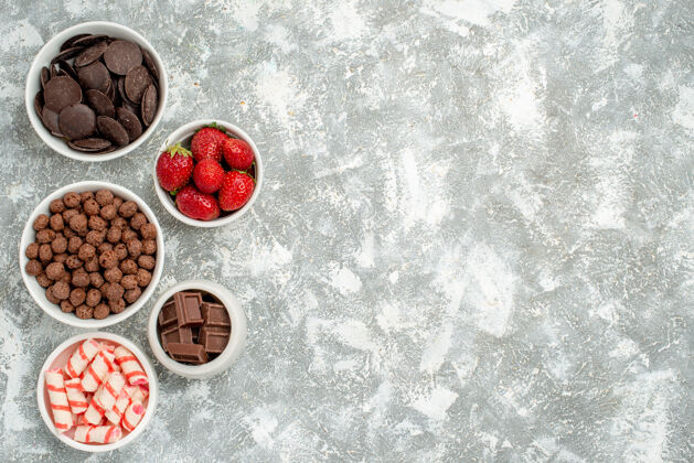 壁板左上角是灰白色地面上放着糖果 草莓 苦味和奶白色巧克力 麦片和可可的碗雪水浆果
