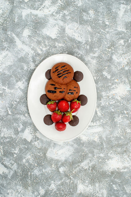 盘子顶远景巧克力饼干草莓和圆巧克力在白色椭圆形盘子上的灰白色地面甜点蓝莓红醋栗