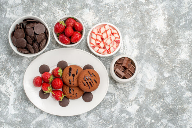 甜点左上角是白色椭圆形盘子上的饼干 草莓和圆形巧克力 在地的左侧 碗里放着糖果 草莓和巧克力壁板地面椭圆形