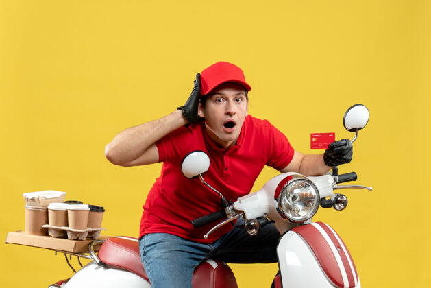 命令一个穿着红色上衣 戴着帽子手套 戴着医用口罩的快递员坐在滑板车上 出示银行卡手套摩托车人