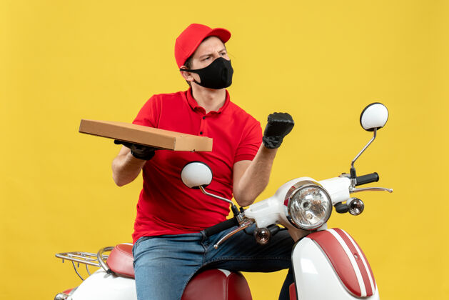 男性俯视图：情绪激动的野心勃勃的快递员身穿红色上衣 戴着帽子手套 戴着医用面罩 坐在滑板车上显示秩序摩托车表演手套