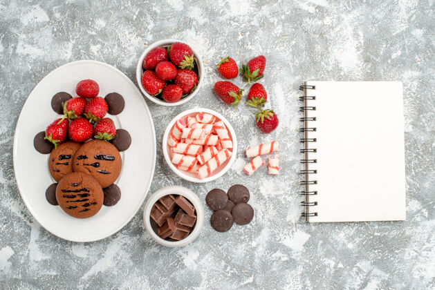 甜点白色椭圆形盘子上的饼干草莓和圆巧克力灰白色桌子上的糖果草莓巧克力和笔记本碗巧克力糖果托盘