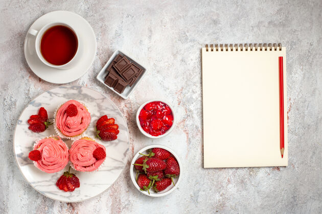桌子白色表面上粉红色草莓蛋糕加奶油和一杯茶的俯视图食物茶水果