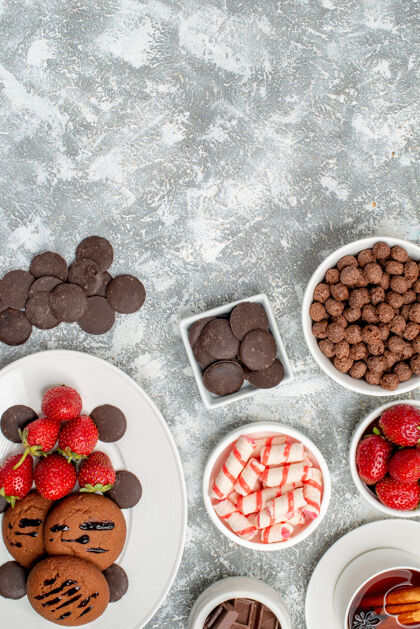 底部顶视图饼干草莓和圆形巧克力放在椭圆形盘子碗里 糖果草莓巧克力谷类食品和一杯茶放在灰白色的桌子底部杯子食物水果