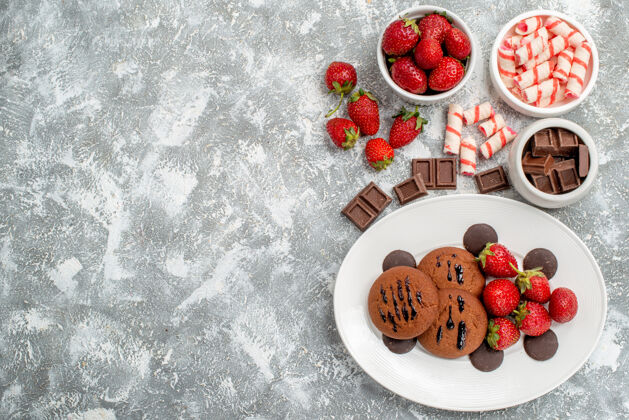 椭圆形白色椭圆形盘子上的饼干草莓和圆形巧克力 灰白色桌子右侧的碗糖果草莓巧克力食物盘子桌子