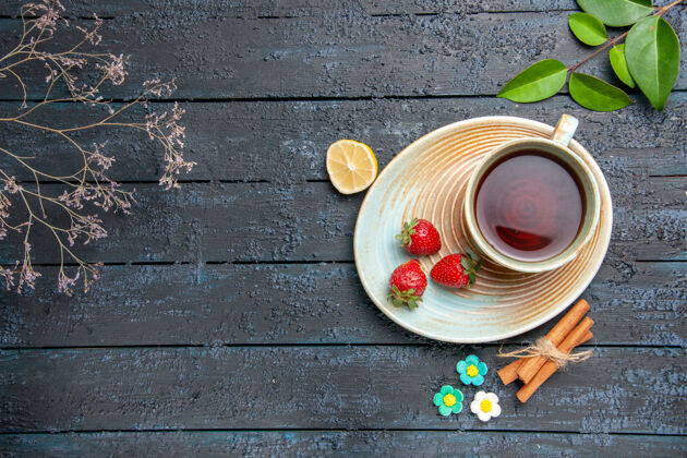 盘子顶视图一杯茶和草莓放在茶碟上柠檬肉桂花糖果片叶子放在深色的木桌上容器肉桂勺子