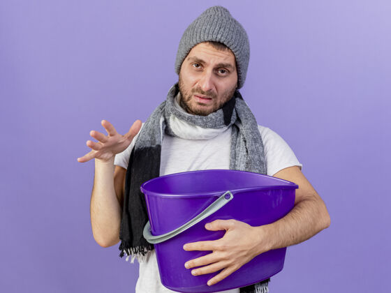 塑料悲伤的年轻人戴着冬天的帽子 戴着围巾 手里拿着塑料桶 孤零零地站在紫色地上水桶帽子年轻