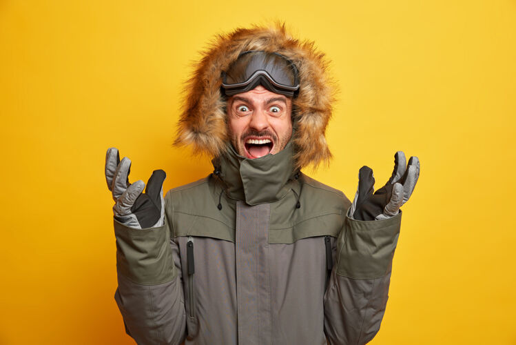 穿着情绪激动的滑雪板运动员举手大声喊叫表达负面情绪穿着冬季夹克带滑雪镜手套手势积极张嘴季节活动寒冷