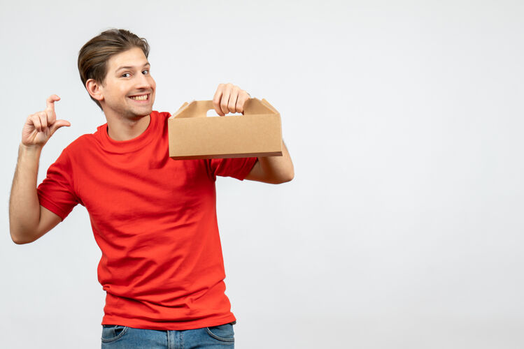 男人顶视图微笑的年轻人在红色衬衫举行的箱子 使确切的东西在白墙上男性成人衬衫