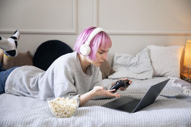 游戏粉红色头发的年轻女子在玩笔记本电脑上的操纵杆玩家玩家室内