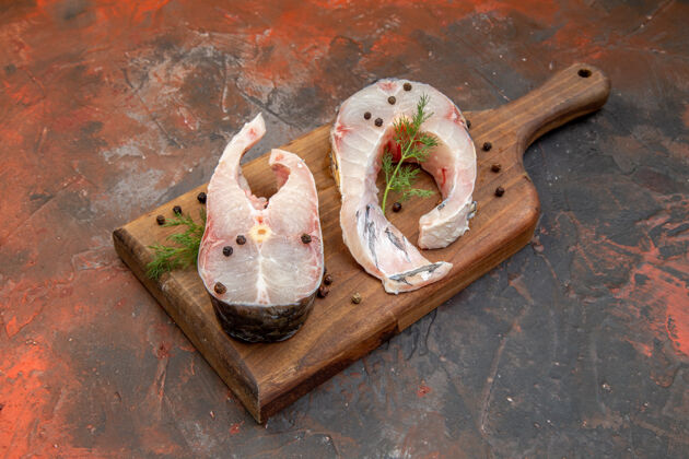 胡椒粉新鲜生鱼肉和胡椒粉的侧视图在混合色表面的木制切割板上盘子生的鱼食物
