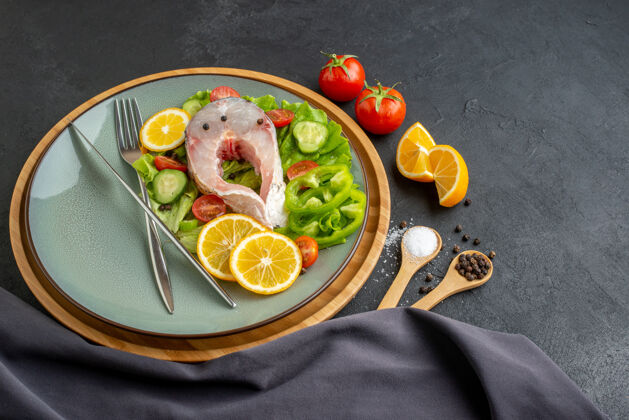 生鱼生鱼片和新鲜蔬菜的侧视图柠檬片和餐具放在灰色盘子上香料深色毛巾放在黑色表面上毛巾壁板盘子