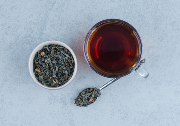 配料一碗干茶叶和一杯用勺子放在大理石上的茶温暖美味新鲜酿造