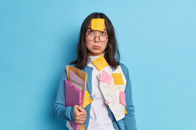 闷闷不乐不开心疲倦的亚洲学生集中在上面有悲伤的表情戴眼镜矫正视力拿着文件夹文件卡着回形针女人压力忧郁