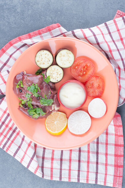 生的生肉和新鲜蔬菜片放在橙色盘子里柠檬牛排食物