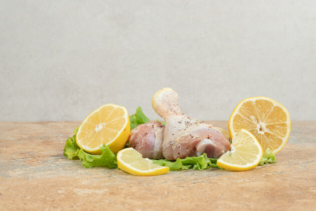 腿生鸡腿配柠檬片和生菜放在大理石表面可口美味未经料理的