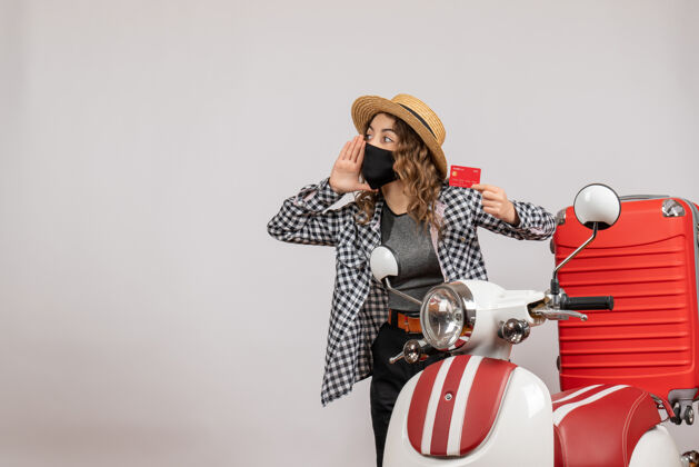 装备站在红色轻便摩托车旁 戴着黑色面具 手持车票的酷女孩的正面图前面乐趣节日