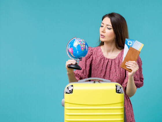 女人前景度假女性手持地球仪和机票在蓝色背景海上度假女性旅行避暑旅程举行蓝色