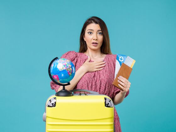 风景正面图：度假中的女性手持蓝色背景的机票出海旅行度假女性出海旅行旅行人前面