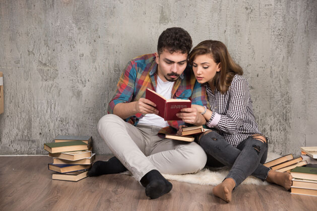 肖像一对年轻夫妇坐在地板上看一本有趣的书女人坐着讨论