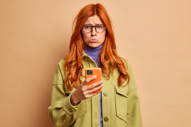 呼叫心灰意冷的欧洲红发女子心烦意乱的男朋友不打电话给看台生气的用手机上网穿绿色夹克失望表情棕色