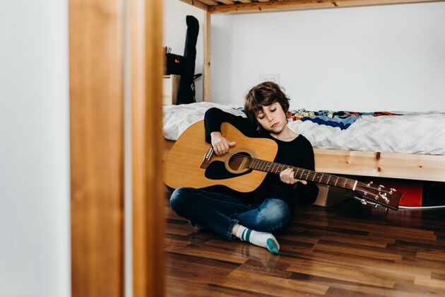 演奏年轻的金发男孩坐在地板上拿着吉他播放器青年乐趣