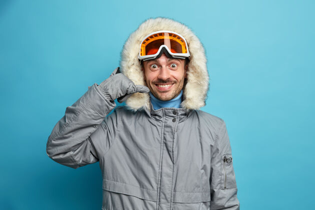 季节快乐的男滑雪运动员穿着带兜帽的冬季夹克 打电话的姿势积极地微笑着休闲年轻人穿